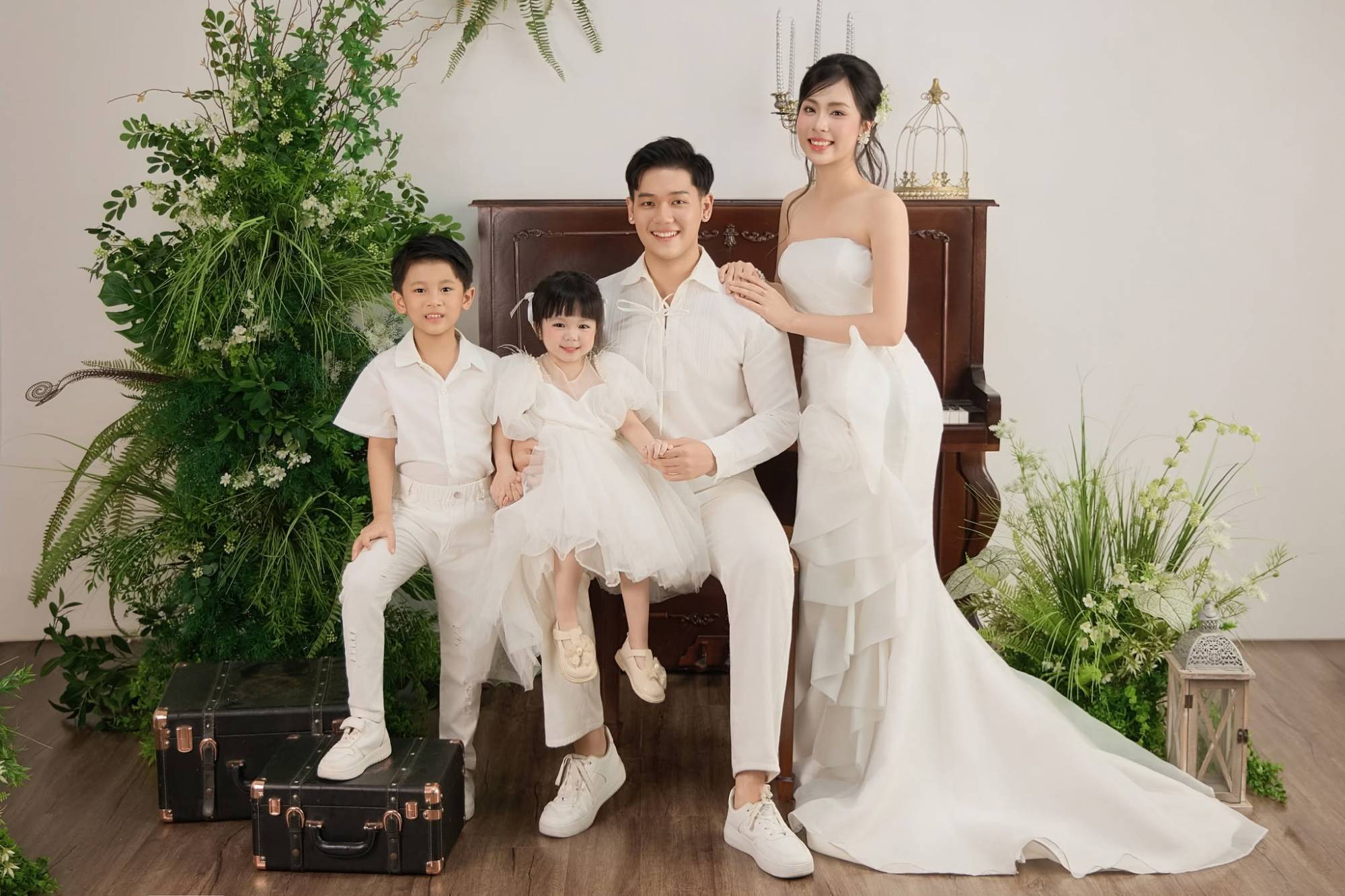 Gia đình bốn người áo trắng bên đàn piano và cây xanh